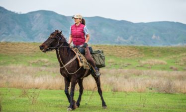 Female rider on a black Tushetian horse in the wide steppe landscape of Vashlovani National Park with the Caucasus in the background