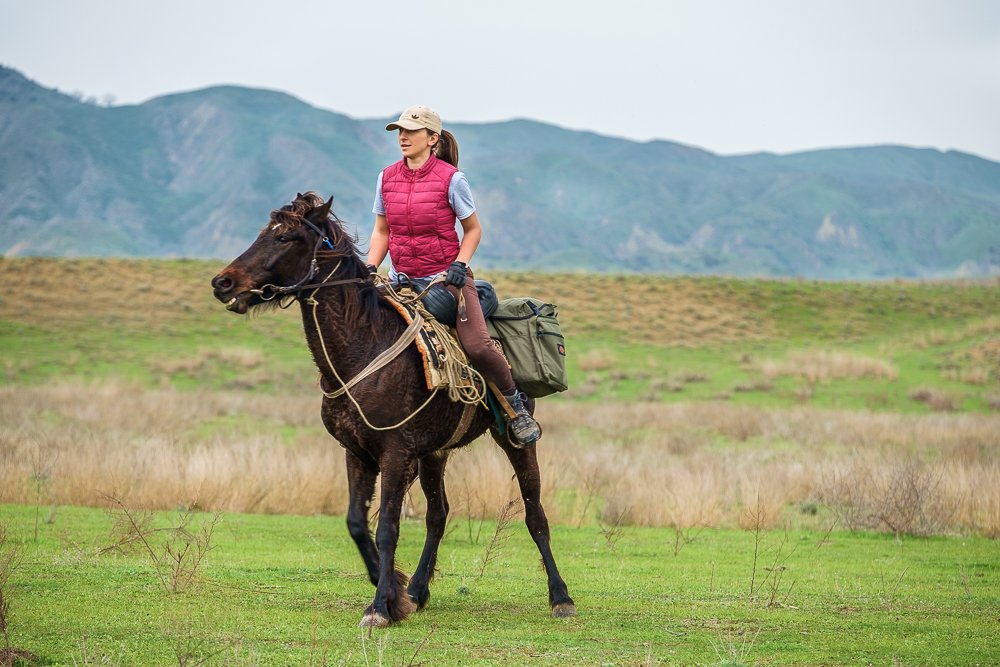 Female rider on a black Tushetian horse in the wide steppe landscape of Vashlovani National Park with the Caucasus in the background