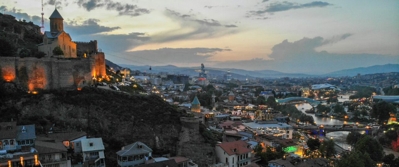 Panoramic view of Tbilisi's old town at dusk with the illuminated Narikala Fortress, Metekhi Church, the Peace Bridge over the Mtkvari River and the modern city skyline in the background, Georgia