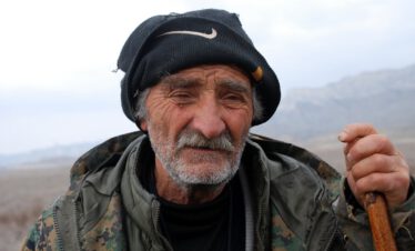 Close-up portrait of an old Tushetian shepherd with hat and stick in the steppe of Vashlovani National Park, Georgia