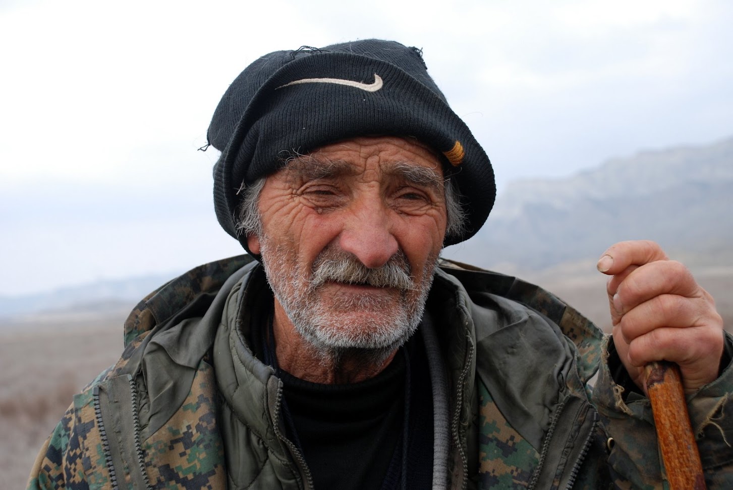 Close-up portrait of an old Tushetian shepherd with hat and stick in the steppe of Vashlovani National Park, Georgia