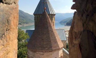 Medieval church tower of Ananuri fortress seen through a stone arch, with the turquoise Jinvali Reservoir in the background, Georgia