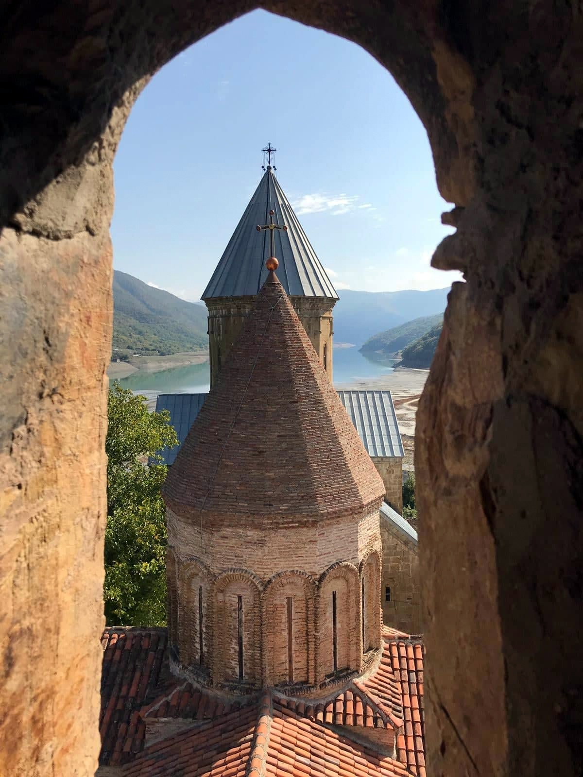Medieval church tower of Ananuri fortress seen through a stone arch, with the turquoise Jinvali Reservoir in the background, Georgia