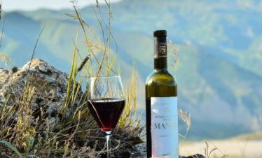Bottle of Azerbaijani pomegranate wine Manat with a glass of red wine on rocks, green Caucasus mountains in the background