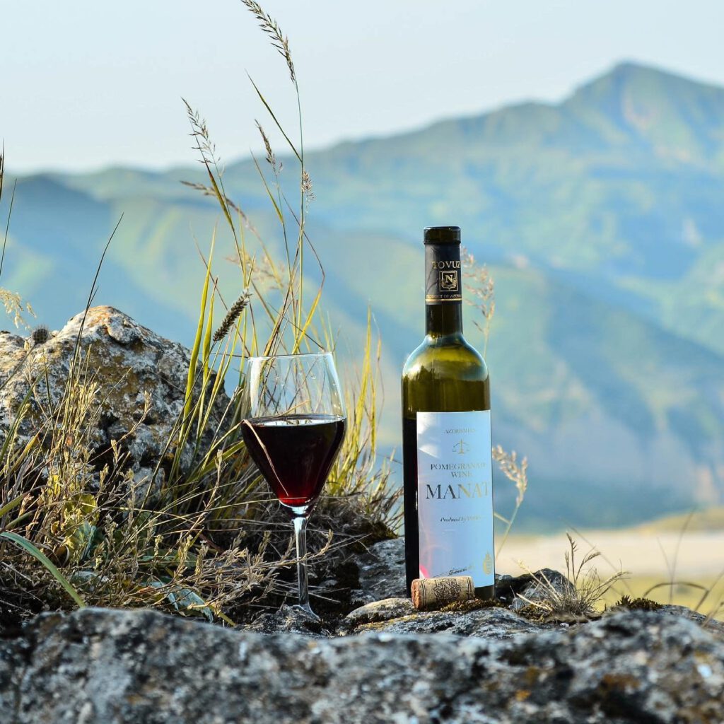 Bottle of Azerbaijani pomegranate wine Manat with a glass of red wine on rocks, green Caucasus mountains in the background