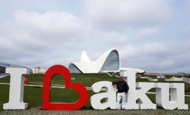 Man standing at the I Love Baku sign in front of the white flowing Heydar Aliyev Center designed by Zaha Hadid, Azerbaijan