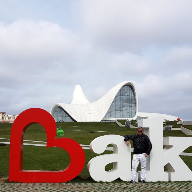 Man standing at the I Love Baku sign in front of the white flowing Heydar Aliyev Center designed by Zaha Hadid, Azerbaijan