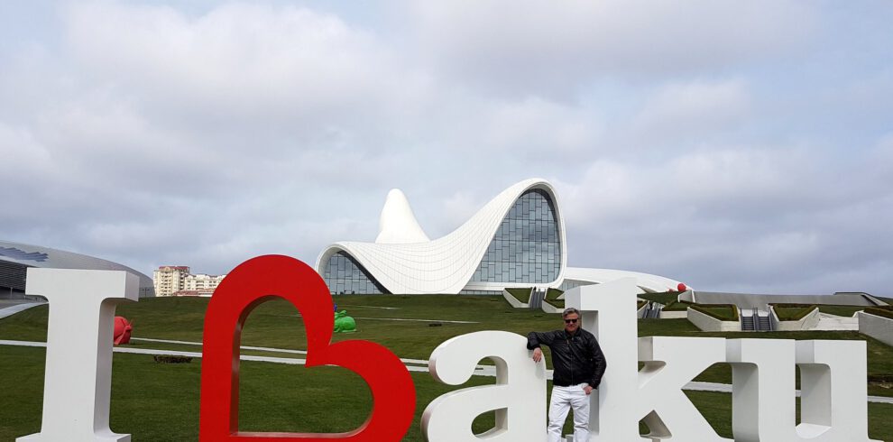 Man standing at the I Love Baku sign in front of the white flowing Heydar Aliyev Center designed by Zaha Hadid, Azerbaijan