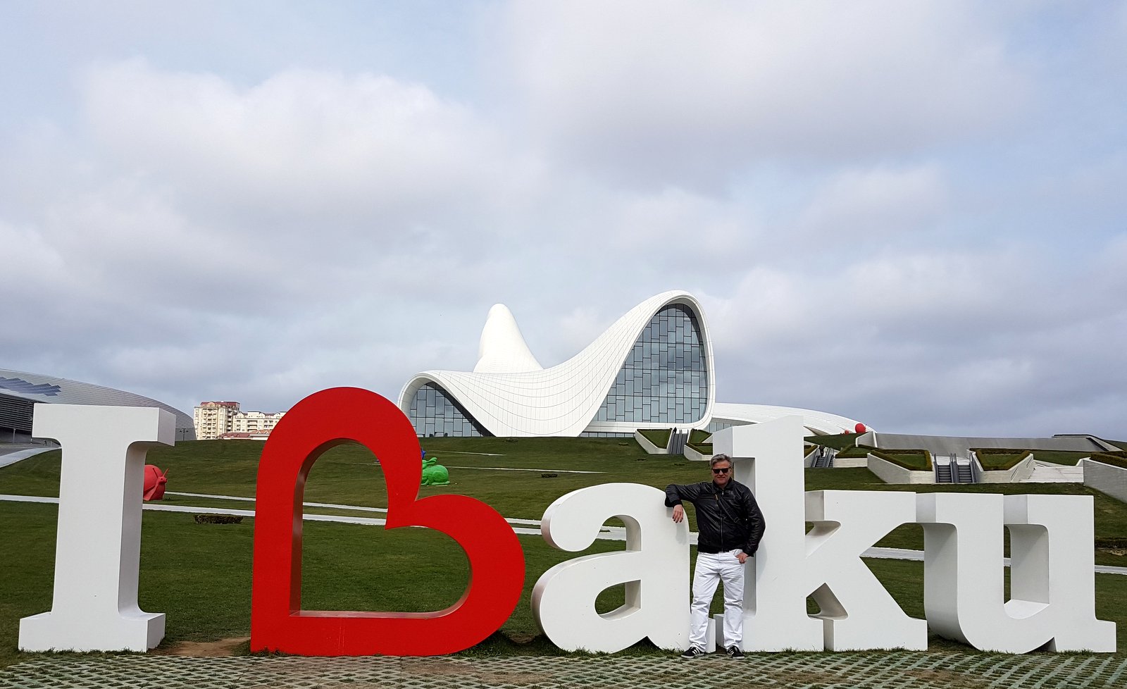 Man standing at the I Love Baku sign in front of the white flowing Heydar Aliyev Center designed by Zaha Hadid, Azerbaijan