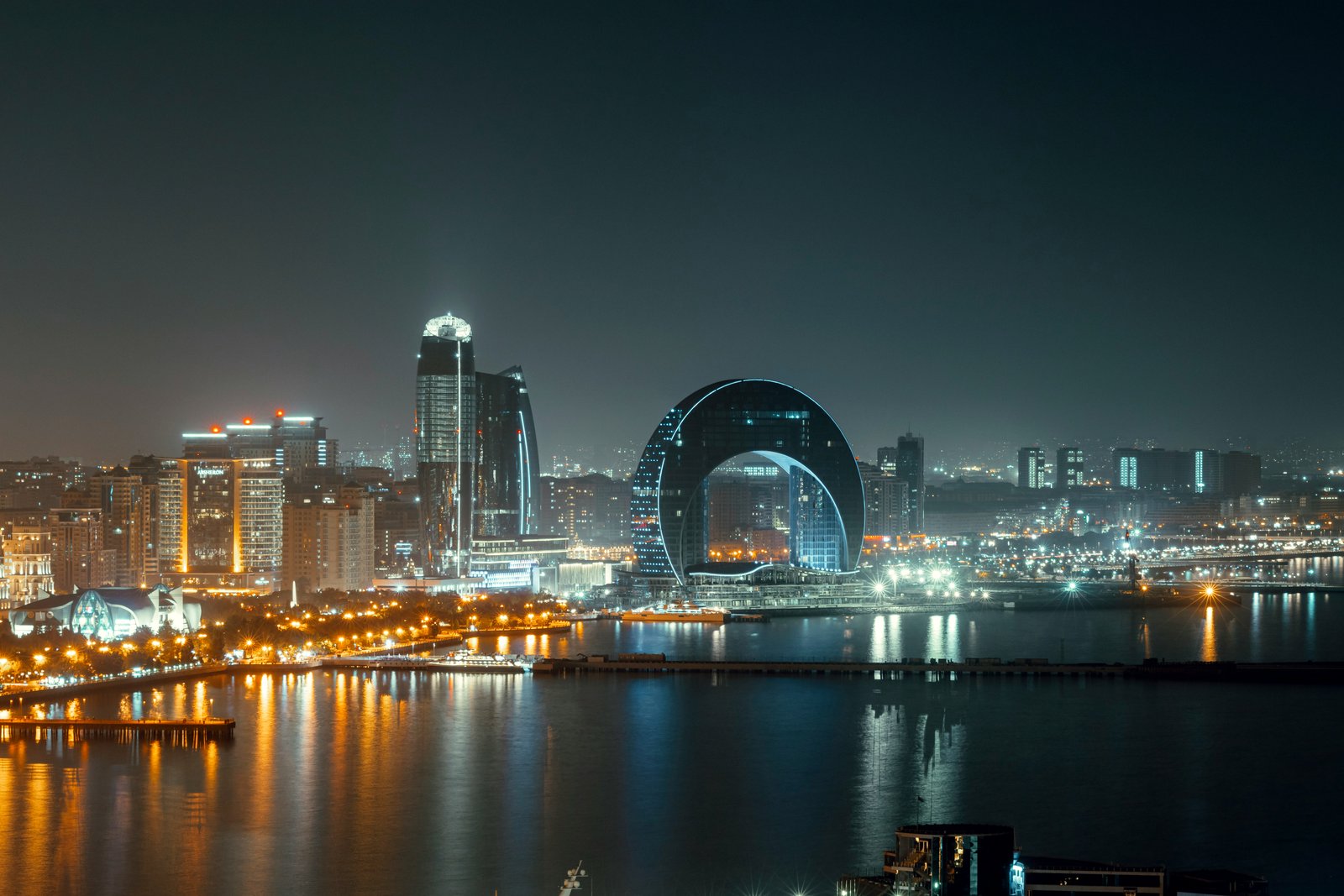 Baku night skyline with illuminated modern skyscrapers and the Caspian Eye Ferris wheel reflected in the Caspian Sea, Azerbaijan