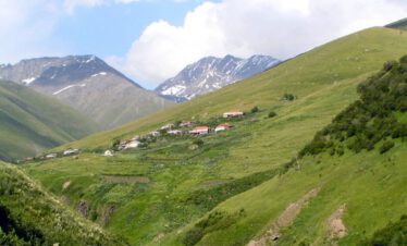Small mountain village of Juta on green alpine slopes with snow-capped peaks of the Chaukhi massif in the background, Sno Valley, Georgia