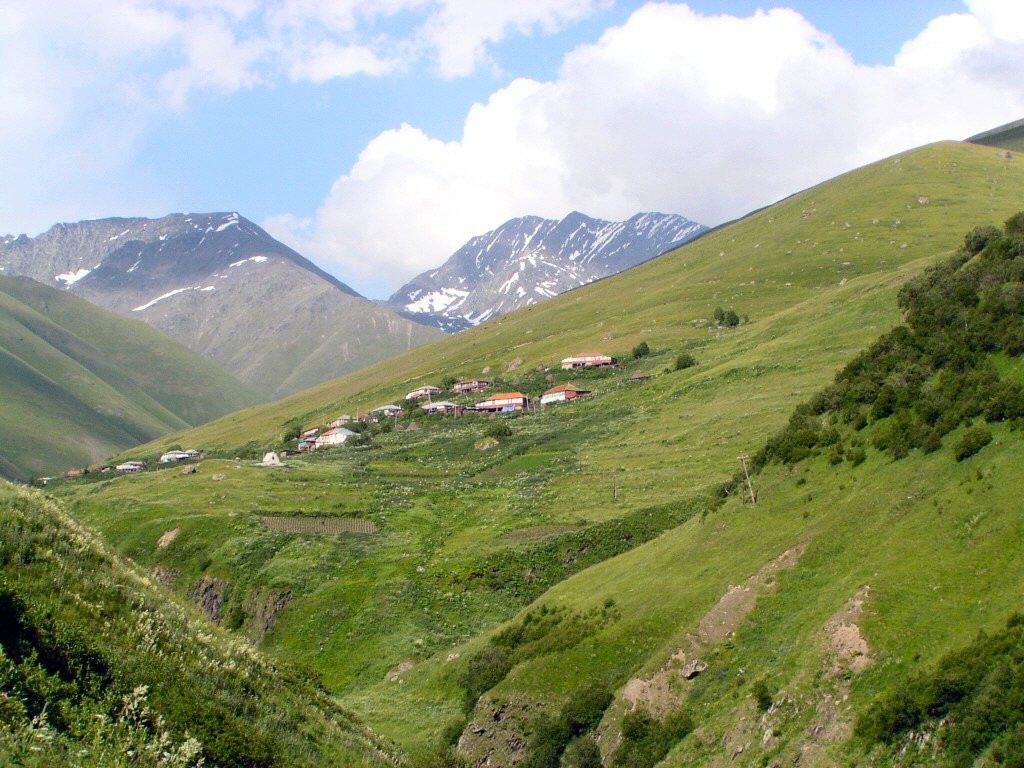 Small mountain village of Juta on green alpine slopes with snow-capped peaks of the Chaukhi massif in the background, Sno Valley, Georgia