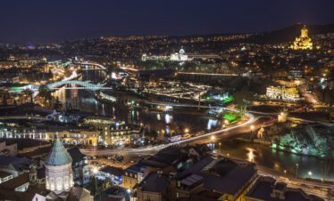 Night panorama of Tbilisi with the illuminated Mtkvari river, the Bridge of Peace and the Sameba Cathedral glowing on the hilltop, Georgia